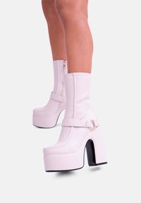 Stivali platform rosa, lucidi, al ginocchio con cinturino e tacco grosso nero, dotati di una cerniera sul retro per un indossamento più facile.