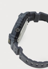Montre numérique grise avec un bracelet en caoutchouc texturé, un dos en acier inoxydable et un bouton lumineux proéminent sur le côté pour plus de fonctionnalité.