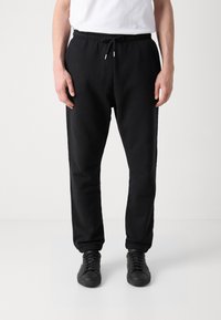 Sorte bomulls joggebukser med elastiske mansjetter og midjebånd. Har snøring og sidelommer. Kombinert med sorte sneakers.