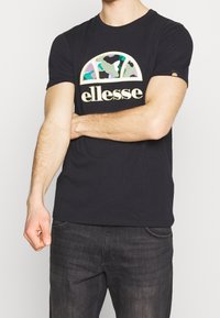 Černé bavlněné tričko s barevným logem s potiskem v maskáčovém vzoru a polokruhovým designem; krátké rukávy a klasický střih.