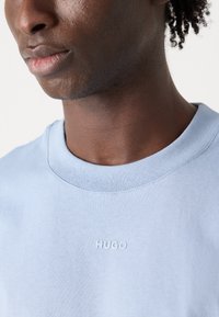 Világoskék pamut póló kerek nyakkivágással, az elején egy diszkrét domború "HUGO" logóval. Simább textúra, laza fazon.