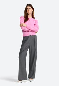 Cardigan rose à côtes avec des manches bouffantes, associé à un pantalon large gris et des chaussures plates blanches. Boutons visibles sur le cardigan.