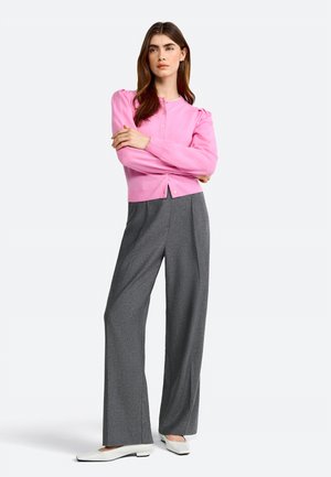 Roze geribde cardigan met pofmouwen, gecombineerd met grijze wijde broekspijpen en witte platte schoenen. Knopen zichtbaar op de cardigan.