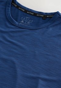 Camiseta activa azul hecha de tejido texturizado. Presenta un escote redondo con una etiqueta negra que muestra "ACTIVE" en el interior del cuello.