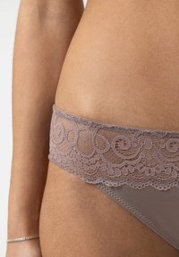 Close-up of a person wearing mauve lace-trimmed underwear, showing detailed floral lace pattern and smooth fabric against skin.