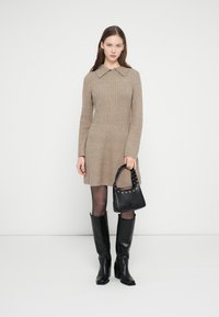 Bézs bordázott kötött ruha galléros nyakkivágással, hosszú ujjakkal és bővülő szegéllyel. Fekete bőr térdig érő csizma és egy kis fekete táska.