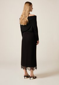 Top negro sin hombros combinado con una falda larga con detalles de encaje en el dobladillo y tacones negros con tiras. Textura suave en todo el conjunto.