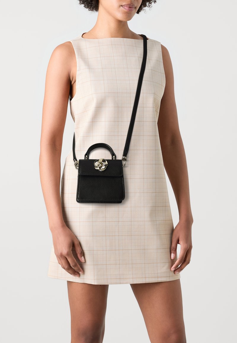 Crna kožna torba s teksturiranom površinom, gornjom ručkom i odvojivim remenom za rame. Ima metalnu cvjetnu kopču. Stil crossbody.