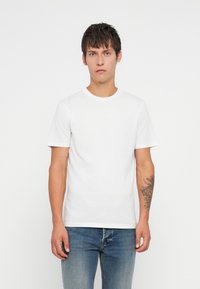 Biały t-shirt z bawełny z krótkim rękawem i okrągłym dekoltem; w połączeniu z jasnoniebieskimi dżinsami; z dyskretnym logo na klatce piersiowej.
