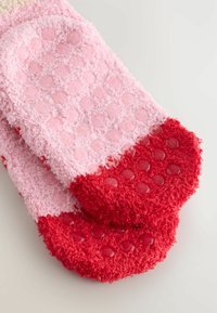Calcetines rosa difusos con una superficie texturizada, puntos de goma roja en la suela y una sección de punta roja vibrante. Textura suave y cálida en general.