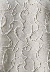 Teksturert stoff i lys beige med hevet, abstrakt kremfarget søm som danner sløyfer og spiraler, og skaper et taktilt design med subtil dimensjon.