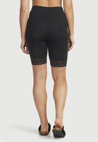 Svarta stretchiga shorts med ett spetsdetalj vid fållen, med resårmidja för komfort. Tyget ser slätt och figurnära ut.