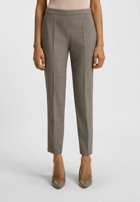 Maßgeschneiderte graue Hose mit subtiler Textur, flachem Vorderteil und zulaufenden Beinen. Kombiniert mit glänzenden neutralen Stilettos.