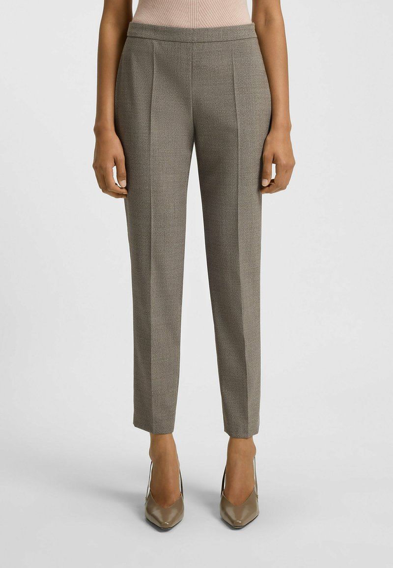 Maßgeschneiderte graue Hose mit subtiler Textur, flachem Vorderteil und zulaufenden Beinen. Kombiniert mit glänzenden neutralen Stilettos.
