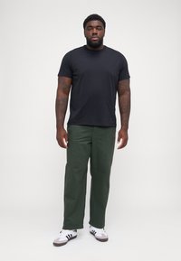 T-shirt noir à manches courtes, pantalon vert à jambes droites, baskets blanches avec accents noirs. Tenue simple et décontractée au design minimaliste.