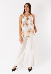 Top senza maniche floreale bianco con rose beige, abbinato a pantaloni larghi color crema e décolleté nere a punta. Tessuto morbido, vestibilità rilassata.