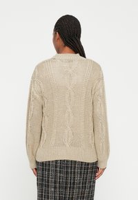 Beige kötött pulóver, kábelmintákkal és bordás mandzsettákkal, kerek nyakkivágással és laza szabással. Texturált anyag, közepes hosszúságú ujjak.