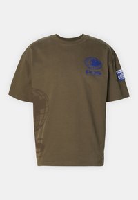 Camiseta de algodón verde oliva con cuello redondo, mangas cortas y estampados gráficos azules de un globo y texto en el frente y la manga.