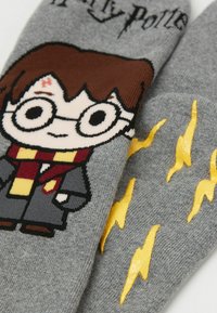 Grau Socken mit einem Cartoon-Charakter, der braune Haare, runde Brillen und einen Schal trägt, neben gelben Blitz-Designs.