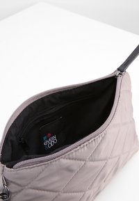 Wytłaczana torebka kopertowa w kolorze mauve z zamkiem błyskawicznym, z czarnym wnętrzem i małą kieszonką, prezentująca markowy metkę w środku.