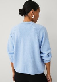 Pull en tricot bleu clair avec une coupe décontractée, manches raglan, et poignets et ourlet côtelés. Texture douce et détail de design décontracté.