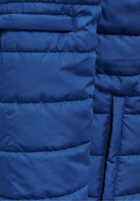 Blå isolerad jacka med quiltad design, med en slät struktur och en sidoficka med dold öppning.