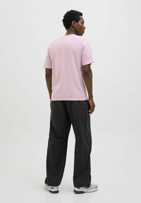 Lyserød kortærmet T-shirt med rund hals, brugt med løstsiddende mørkegrå bukser og hvide sko, set fra ryggen.