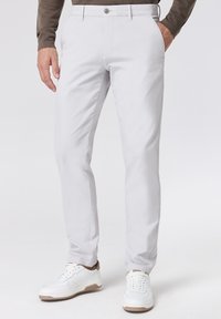 Chinos grigio chiaro con una texture liscia, dotati di chiusura a bottone, tasche laterali e un design slim fit, abbinati a sneakers bianche.