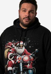 Černá mikina s kapucí, na které je grafika Santa Clause jedoucího na motorce, ozdobená taškou s dárky, v červené a bílé barvě s barevnými akcenty.