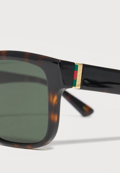 Γυαλιά ηλίου με σκελετό από χελώνα, φακούς με πράσινη απόχρωση και χρυσές λεπτομέρειες στα μαύρα μπράτσα με πράσινες και κόκκινες ρίγες.