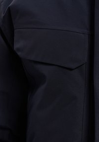 Tamsiai mėlynas švarkas su sulankstomu apykakle ir krūtine kišene. Audinys lygus, matinio paviršiaus, o siuvimo detalės matomos palei siūles.