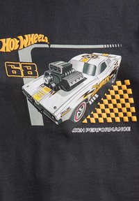 De afbeelding toont een witte retro auto met een grote zwarte motor op een donkere achtergrond. Bevat elementen zoals gele accenten en geblokte patronen.