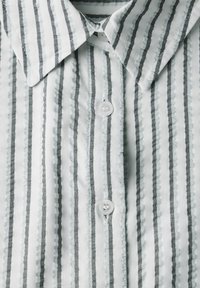 Camicia bianca con sottili righe verticali grigie, colletto a punta e tre bottoni. Tessuto morbido e strutturato con un delicato dettaglio a costine.