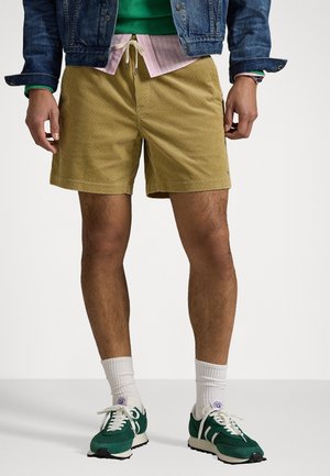 Cordial shorts i sennepsgul med en afslappet pasform, der har en snor i taljen. Blandet med grønne sneakers og hvide sokker.