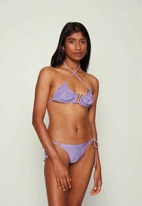 Conjunto de biquíni roxo com top triângulo plissado e detalhe em metal dourado, além de parte de baixo com laços ajustáveis. Textura sedosa.