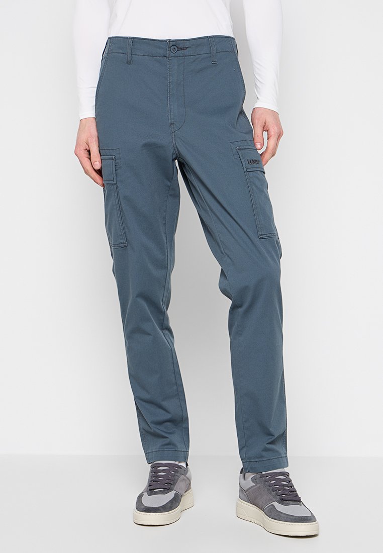 Blaue Cargo-Hosen aus Baumwollmischgewebe, mit Seitentaschen, geradem Schnitt und Knopfverschluss. Tragen Sie dazu graue Turnschuhe.