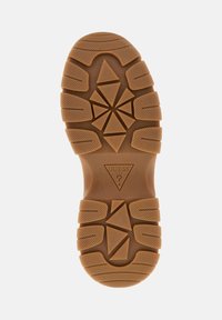 Semelle de chaussure en caoutchouc brun avec une surface texturée, des motifs de bande de roulement angulaires et un logo central en forme triangulaire.