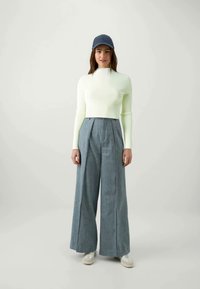 Ljusgrön kortärmad tröja, vida grå byxor med framfåll, och en mörk mössa. Outfiten har en minimalistisk design och slät textur.
