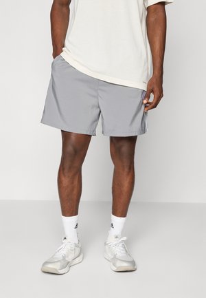 Gray athletic shorts with a loose fit, made from lightweight fabric. Features side pockets and a subtle logo detail. Worn with white socks and sneakers.