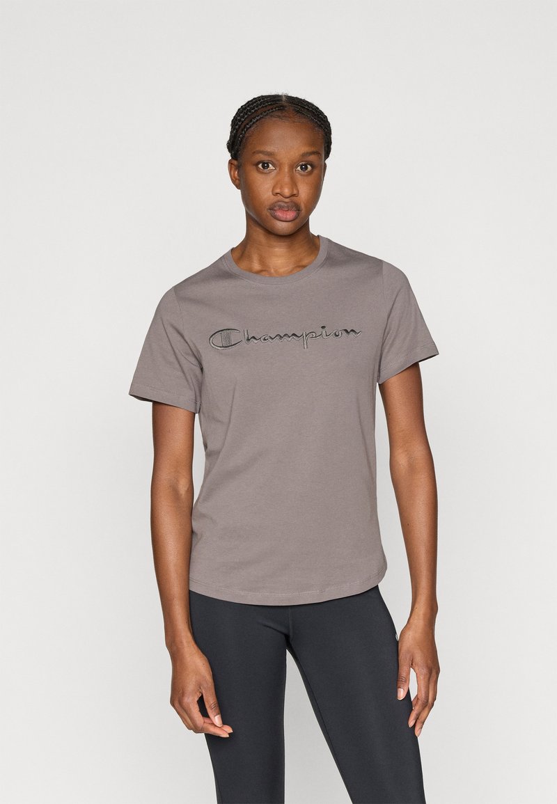 Gray cotton t-shirt with rounded neckline and short sleeves, featuring an embroidered "Champion" logo across the chest. Paired with black leggings.