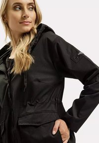 Czarna, lekka kurtka z kapturem, elastycznym pasem i kieszeniami z przodu. Posiada zamek błyskawiczny oraz małe logo na rękawie.