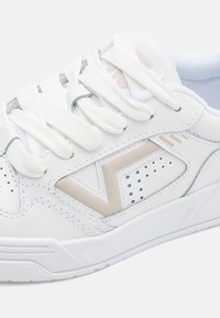Tenis alb cu superior din piele, cu un design geometric bej, sireturi albe, perforații pentru ventilație și o talpă texturată.