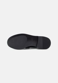 Talpa neagră de pantof, fabricată din cauciuc neted, având un design plat cu textură antiderapantă și numele mărcii embosat aproape de călcâi.
