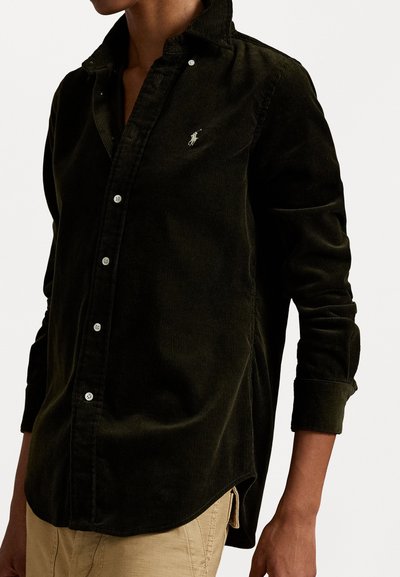 Green corduroy shirt with button-down collar, front buttons, and a small logo on the chest. Features long sleeves and side slits at the hem.