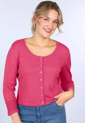 Fuchsia cardigan with a scoop neckline and seven buttons. Three-quarter sleeves feature a textured accent. Worn with blue jeans.