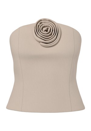 Donna con capelli ricci che indossa un completo beige composto da top senza spalline e pantaloni con dettagli a forma di rosa, che cammina su pavimento grigio su sfondo bianco.