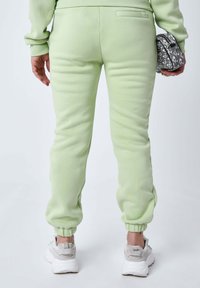 Pantalones deportivos verde claro con pierna ajustada y puños elásticos, que cuentan con un detalle de bolsillo trasero y se llevan con zapatillas blancas.