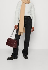 Henkilö, joka käyttää vaaleanharmaata neuletta, mustia farkkuja, mustia kenkiä kultaisilla yksityiskohdilla, beigeä huivia, ja pitää tummanpunaisen päällystetyn käsilaukun, jossa on ketjumaiset hihnat.