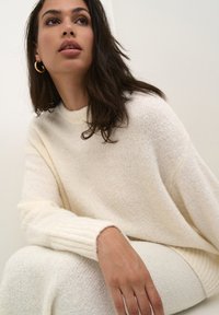 Oversized crèmekleurige trui van zacht, textuur gebreid materiaal met ribbelmanchetten, gecombineerd met een bijpassende crèmekleurige gebreide onderkant. Eenvoudig en comfortabel ontwerp.