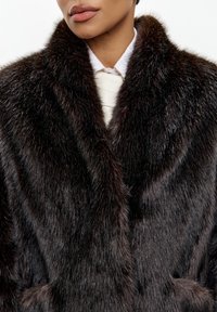 Brun faux fur frakke med en blød tekstur, bred krave og dyb, rig farve. Har et klassisk design med en sjal-lignende halsudskæring.